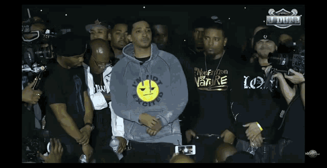 a man wearing a hoodie with a smiley face on it is surrounded by other men