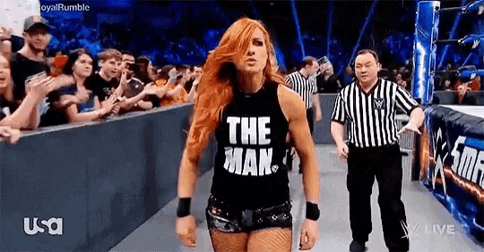 a woman is wearing a tank top that says `` the man '' while walking in a wrestling ring .