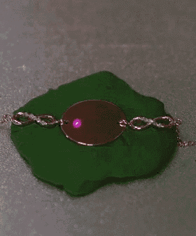 a bracelet with a pink stone on it is on a green surface