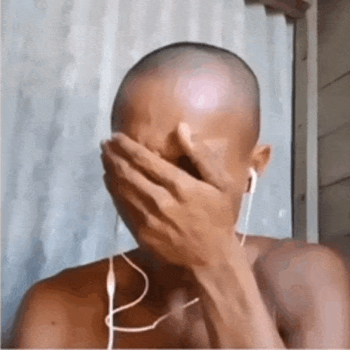 a man with a shaved head is covering his face with his hand while wearing headphones .