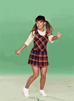a woman in a plaid dress and white sneakers is dancing on a green background .