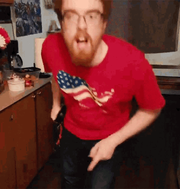 a man in a red shirt with an american flag on it is standing in a kitchen