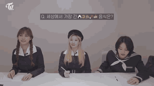 three girls are sitting at a table with a sign that says toi