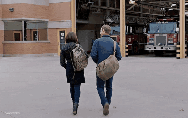 a man and a woman are walking in front of a fire truck number 81