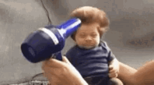 a baby is getting his hair blow dried by a person .