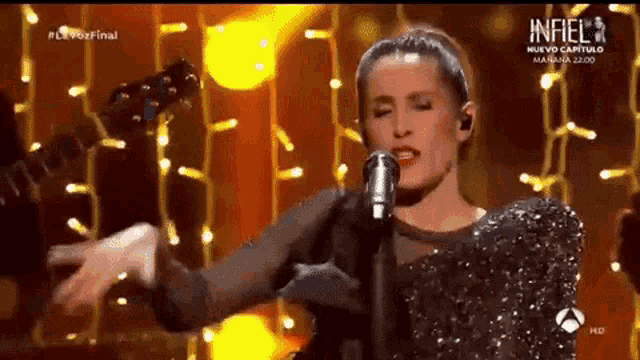 a woman singing into a microphone on a stage with a sign that says infiel