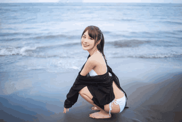 a woman in a bikini is squatting down on the beach