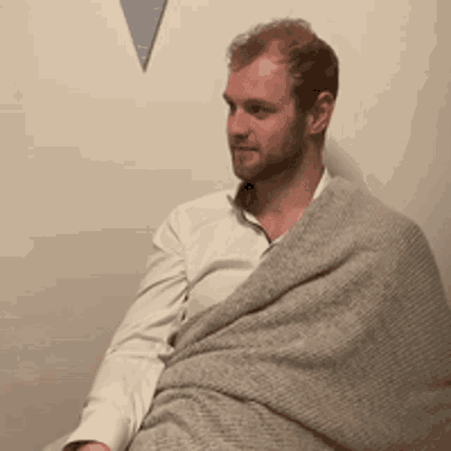 a man wrapped in a grey blanket is sitting on a chair