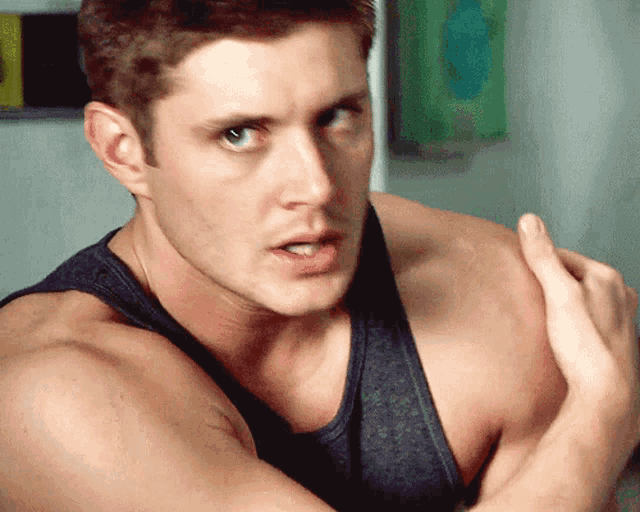 a man in a black tank top is flexing his muscles and looking at the camera