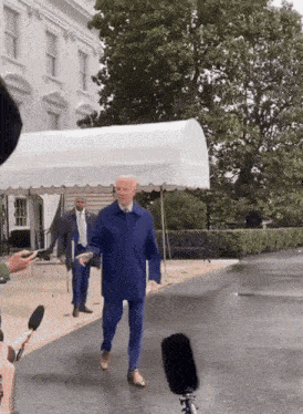 a man in a blue suit is walking in front of the white house