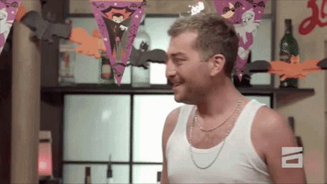 a man wearing a white tank top is smiling in front of a wall with halloween decorations