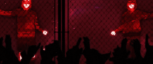 a man in a red hoodie is standing in front of a crowd of people behind a chain link fence .