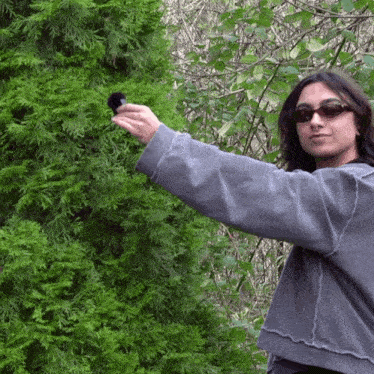a woman wearing sunglasses is holding a black object in front of a tree