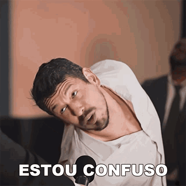 a man in a white shirt stands in front of a microphone with the words " estou confuso " behind him