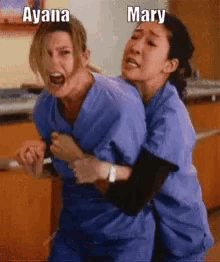 two women in scrubs are hugging each other and one of them is screaming while the other is laughing .
