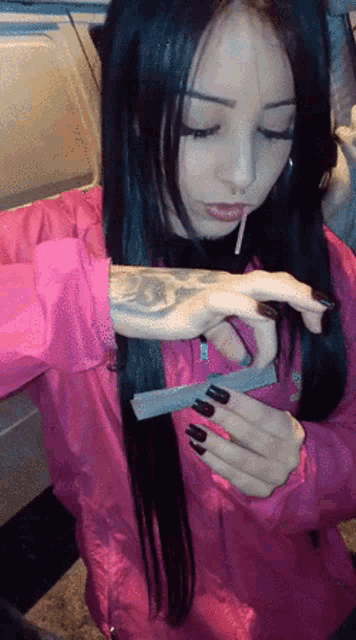 a woman in a pink jacket is holding a cigarette in her mouth
