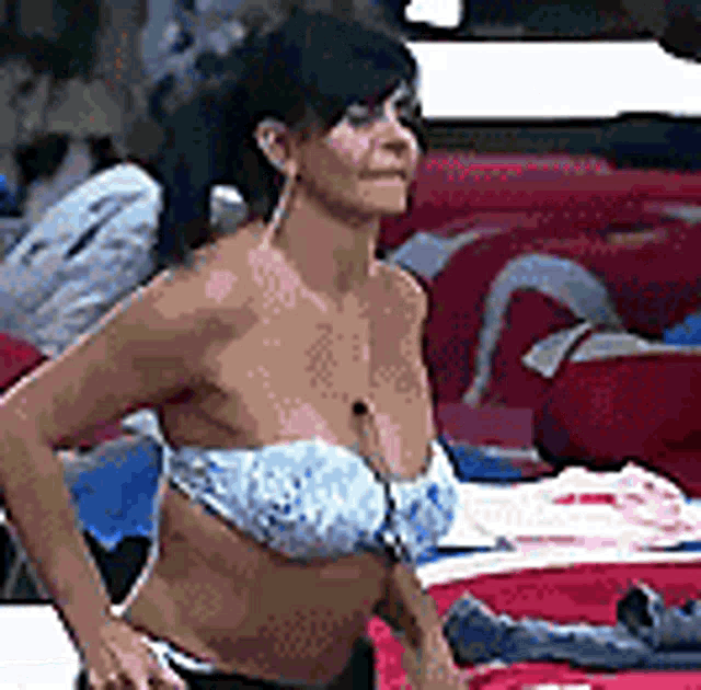 a woman in a bikini is standing in front of a pile of clothes on a bed .
