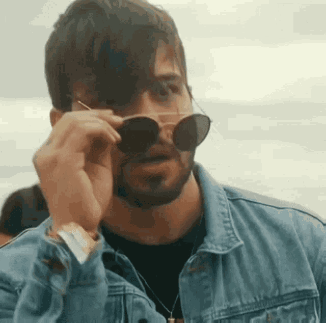 a man with a beard wearing sunglasses and a denim jacket .