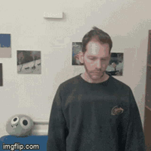 a man in a black shirt is standing in front of a wall with pictures on it .