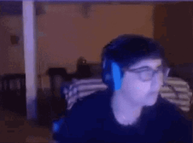 a man wearing headphones and glasses looks at the camera in a dark room