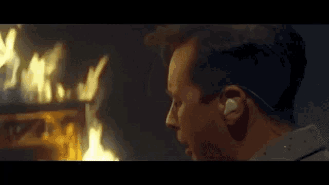 a man wearing headphones is looking at a fire in the background .