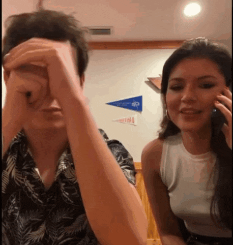 a man covering his face while a woman talks on a phone