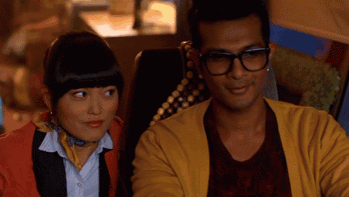 a man wearing glasses and a yellow cardigan sits next to a woman wearing a scarf