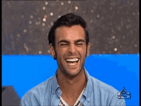 a man in a blue shirt is smiling while sitting in front of a blue background .