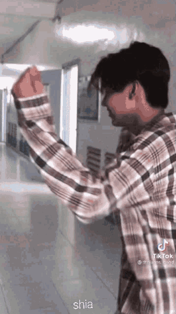 a man in a plaid shirt is standing in a hallway with his fist in the air and shia written below him