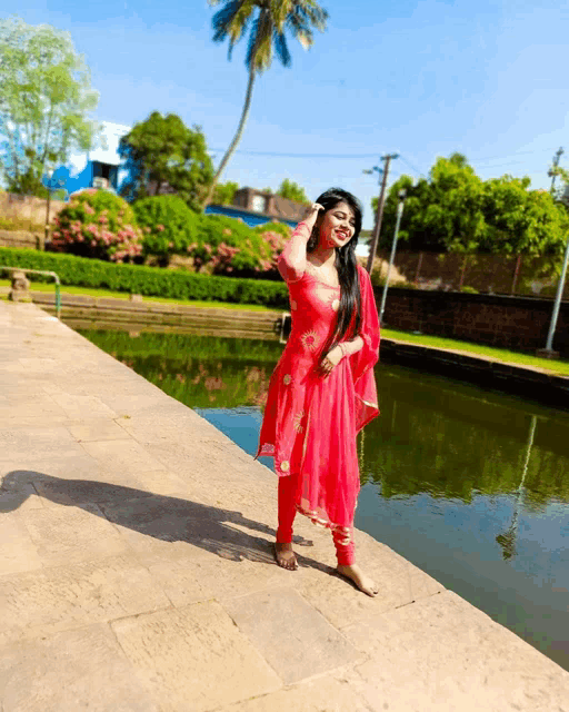 a woman in a red dress is standing next to a pond