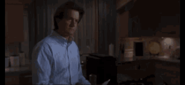 a man in a blue shirt is standing in a dark kitchen
