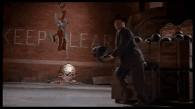 a man in a suit is holding a bowling ball in front of a sign that says keep clear .