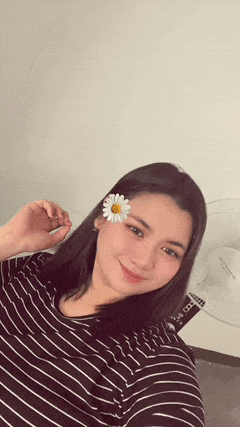 a woman wearing a striped shirt with a flower in her hair is taking a selfie .