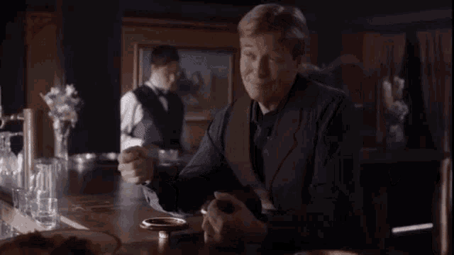 a man in a vest is sitting at a bar talking to another man