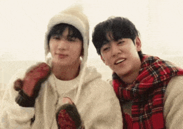 two young men are sitting next to each other wearing scarves and mittens .