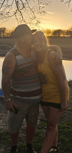 a man and a woman are posing for a picture in front of a lake at sunset