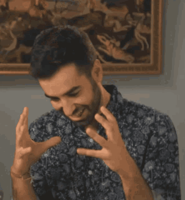 a man with a beard is making a gesture with his hands in front of a framed painting