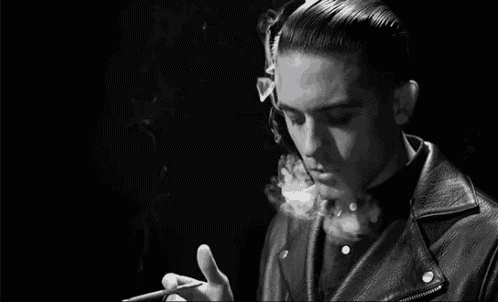 a young man in a leather jacket is smoking a cigarette .
