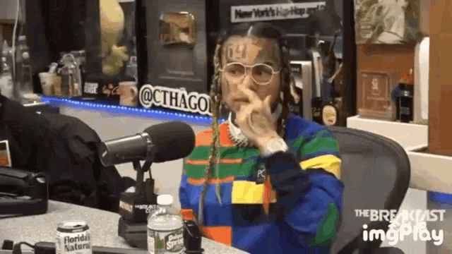 a man with a tattoo on his face is sitting in front of a microphone in a studio .