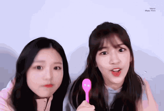 two girls are standing next to each other and one is holding a pink spoon