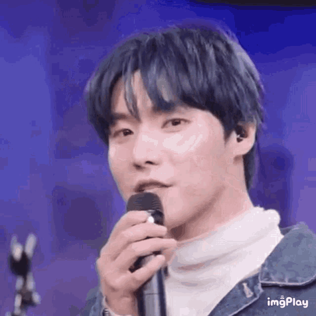 a man with blue hair is holding a microphone in his hand .