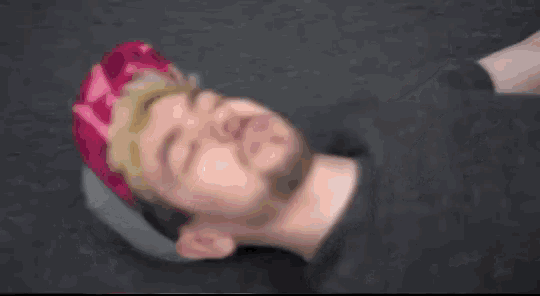 a man with a beard and a pink hat is laying on the floor with his eyes closed .
