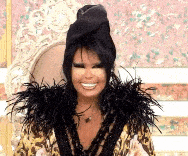 a woman wearing a feathered jacket and a black hat smiles