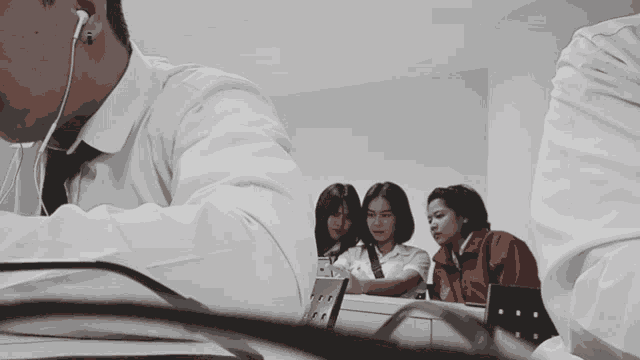 a man wearing ear buds sits at a desk in front of a group of girls