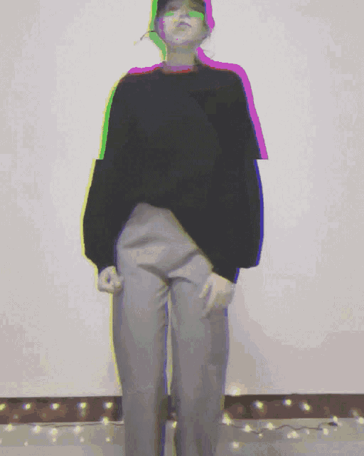 a woman in a black sweater and grey pants is standing in front of a wall
