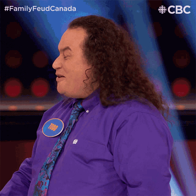 a man with long curly hair wearing a purple shirt and tie with a name tag that says mike