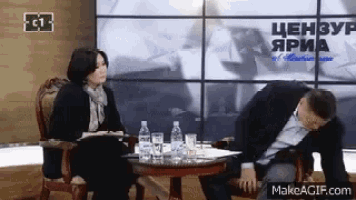 a man and a woman are sitting at a table with bottles of water and a sign that says " цензуя "