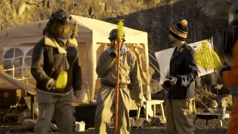 a group of people standing in front of a tent with one man wearing a helmet