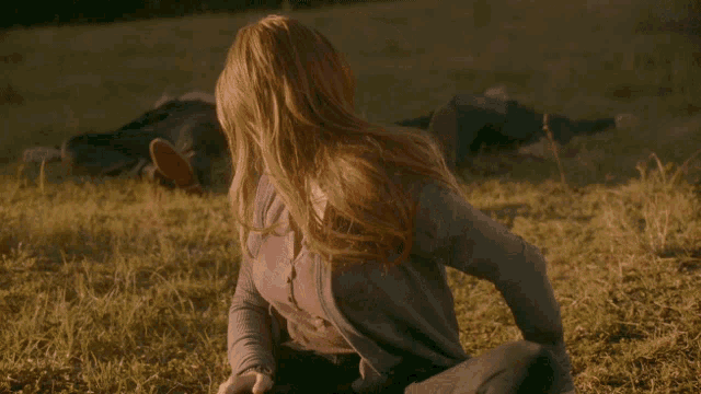 a woman is sitting in the grass looking at something