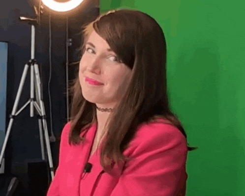 a woman in a pink jacket is sitting in front of a green screen in a studio .